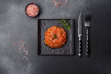 Boiled rice with peppers, spices, herbs and tomato sauce on a black slate plate on a grey concrete background