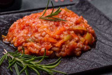 Boiled rice with peppers, spices, herbs and tomato sauce on a black slate plate on a grey concrete background