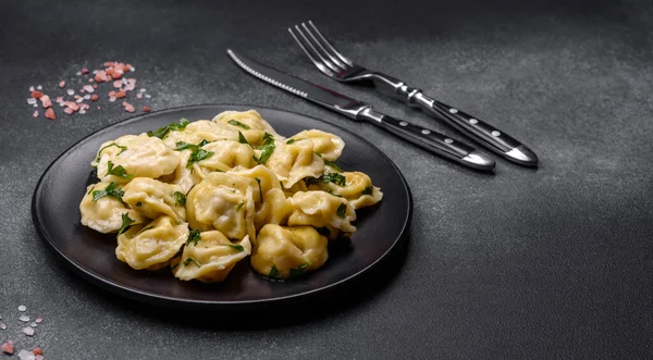 Delicious fresh dumplings with turkey meat, with spices and herbs, parsley on a black plate against a dark concrete background