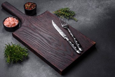 Wooden cutting board, salt, pepper, spices and herbs on a dark concrete background. Cooking delicious home-cooked food