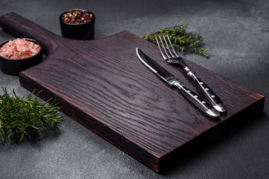 Wooden cutting board, salt, pepper, spices and herbs on a dark concrete background. Cooking delicious home-cooked food