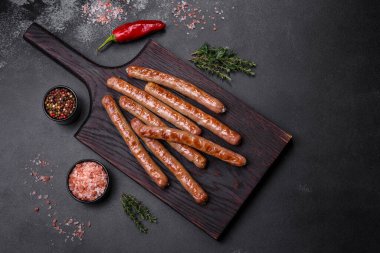 Grilled sausage with the addition of herbs and vegetables on the wooden cutting board. Grilling food, barbecue