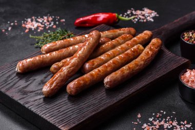 Grilled sausage with the addition of herbs and vegetables on the wooden cutting board. Grilling food, barbecue