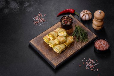 Zucchini appetizer rolls with cream cheese and eggs on a cutting board on dark gray background