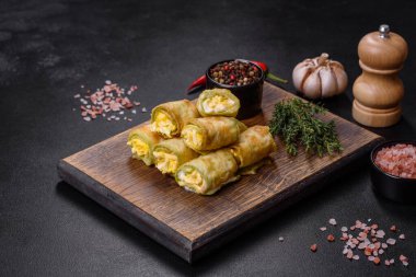 Zucchini appetizer rolls with cream cheese and eggs on a cutting board on dark gray background
