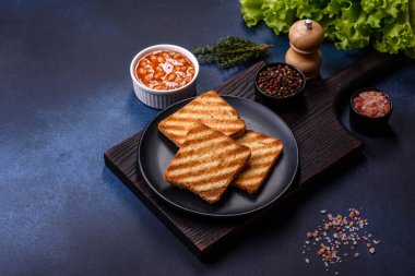 Geleneksel İngiliz kahvaltısı yumurta, tost, sosis, fasulye, baharat ve yeşil seramik tabakta koyu beton arka planda otlar.