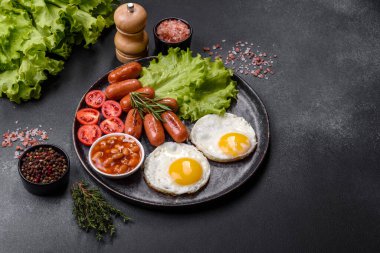 Geleneksel İngiliz kahvaltısı yumurta, tost, sosis, fasulye, baharat ve yeşil seramik tabakta koyu beton arka planda otlar.