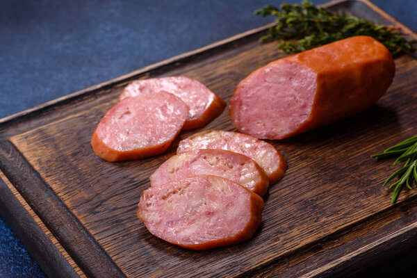Delicious fresh smoked sausages cut with slices on a wooden cutting board against a dark concrete background