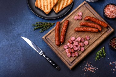 Lezzetli taze füme sosisler tahta kesme tahtasıyla kesilmiş koyu beton bir arka planda.