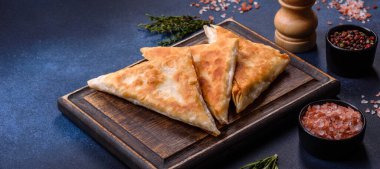 Koyu beton arka planda kesilmiş et ve otlarla ev yapımı cheburekler, geleneksel Kafkas mutfağı.