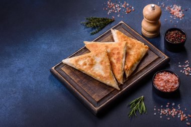 Koyu beton arka planda kesilmiş et ve otlarla ev yapımı cheburekler, geleneksel Kafkas mutfağı.