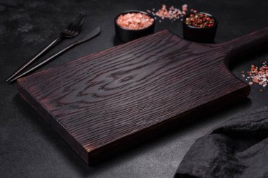 İçinde baharatlar, otlar ve çatal bıçaklar olan koyu beton bir arka planda boş bir siyah tabak. Ev yemeği.