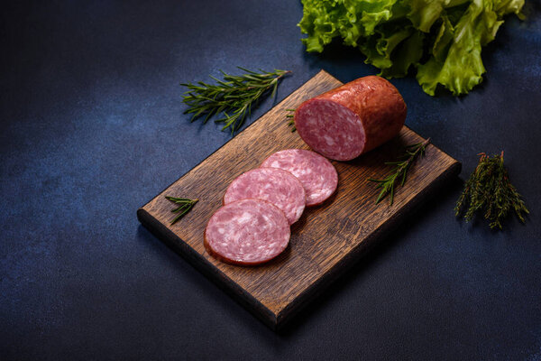 Delicious fresh smoked sausage cut with slices on a wooden cutting board against a dark concrete background
