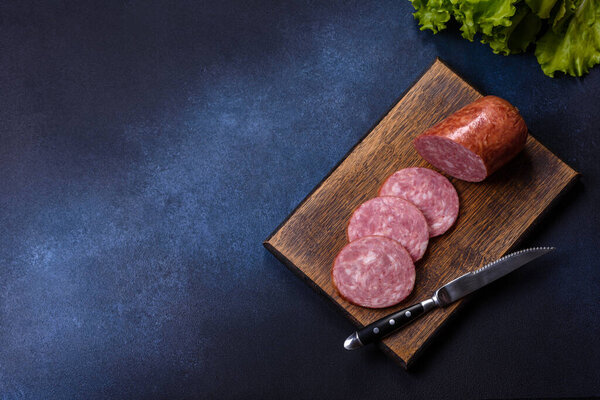 Delicious fresh smoked sausage cut with slices on a wooden cutting board against a dark concrete background