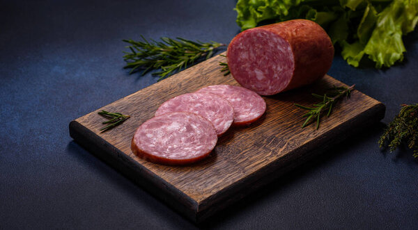 Delicious fresh smoked sausage cut with slices on a wooden cutting board against a dark concrete background