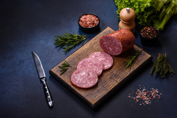 Delicious fresh smoked sausage cut with slices on a wooden cutting board against a dark concrete background