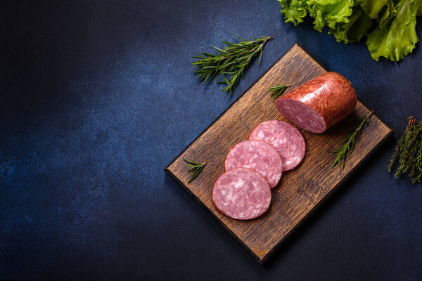Delicious fresh smoked sausage cut with slices on a wooden cutting board against a dark concrete background