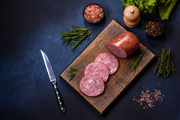 Delicious fresh smoked sausage cut with slices on a wooden cutting board against a dark concrete background