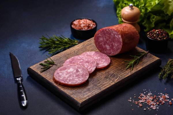 Delicious fresh smoked sausage cut with slices on a wooden cutting board against a dark concrete background
