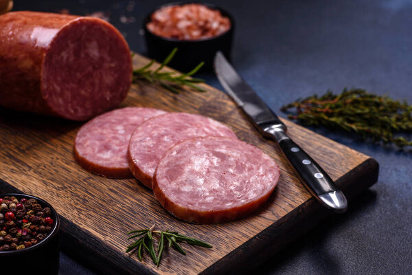 Delicious fresh smoked sausage cut with slices on a wooden cutting board against a dark concrete background