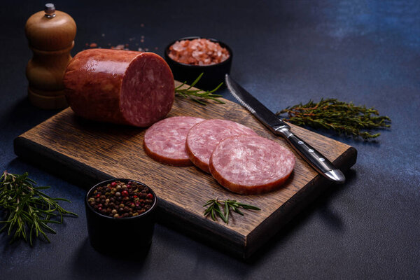 Delicious fresh smoked sausage cut with slices on a wooden cutting board against a dark concrete background