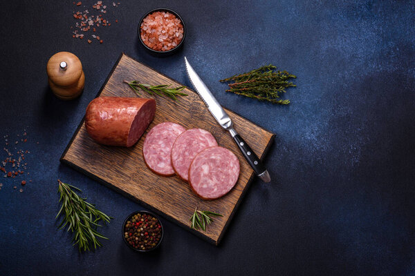 Delicious fresh smoked sausage cut with slices on a wooden cutting board against a dark concrete background
