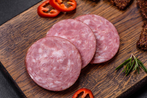 Delicious fresh smoked sausage cut with slices on a wooden cutting board against a dark concrete background