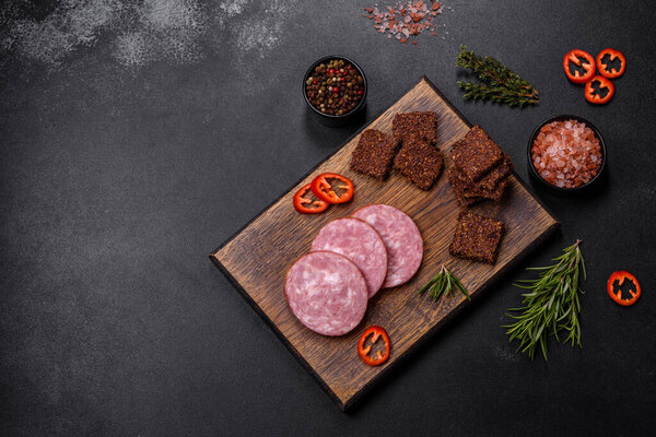 Delicious fresh smoked sausage cut with slices on a wooden cutting board against a dark concrete background