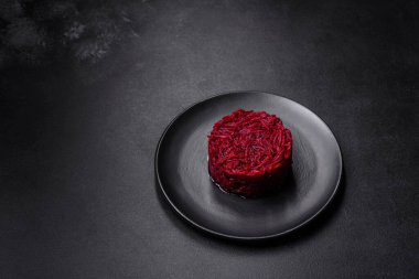 Kavrulmuş pancar kökü silindir şeklinde ve siyah bir tabakta koyu beton bir zemine karşı hazır.