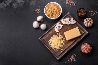 Çiğ makarna, mantar, soğan, kıyma, baharat ve otlar, domates soslu lezzetli bir macun yapmak için koyu beton arka planda.