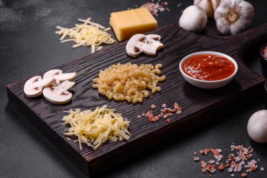 Çiğ makarna, mantar, soğan, kıyma, baharat ve otlar, domates soslu lezzetli bir macun yapmak için koyu beton arka planda.