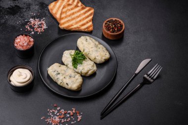 Geleneksel Litvanya yemeği zeplini, haşlanmış patates köfteleri kıyma ile doldurulmuş siyah seramik tabakta koyu beton arka planda.