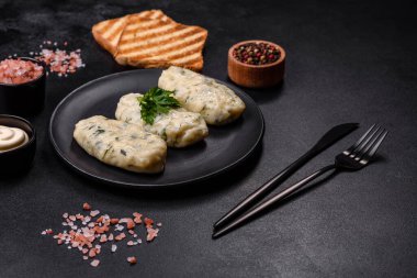 Geleneksel Litvanya yemeği zeplini, haşlanmış patates köfteleri kıyma ile doldurulmuş siyah seramik tabakta koyu beton arka planda.