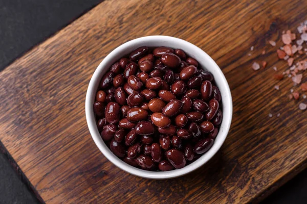 Black, canned beans in a white saucer against a dark concrete background. Ingrient for vegitarian cooking