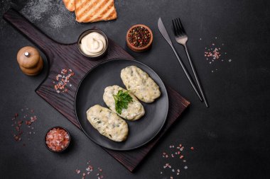 Geleneksel Litvanya yemeği zeplini, haşlanmış patates köfteleri kıyma ile doldurulmuş siyah seramik tabakta koyu beton arka planda.