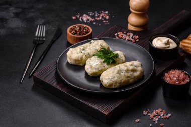 Geleneksel Litvanya yemeği zeplini, haşlanmış patates köfteleri kıyma ile doldurulmuş siyah seramik tabakta koyu beton arka planda.