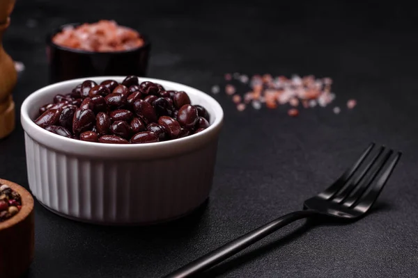 Black, canned beans in a white saucer against a dark concrete background. Ingrient for vegitarian cooking