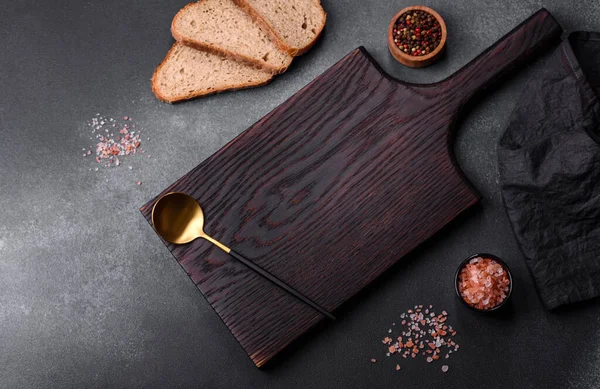 Black rectangular wooden cutting board with salt and spices on a dark concrete background. Cooking at home