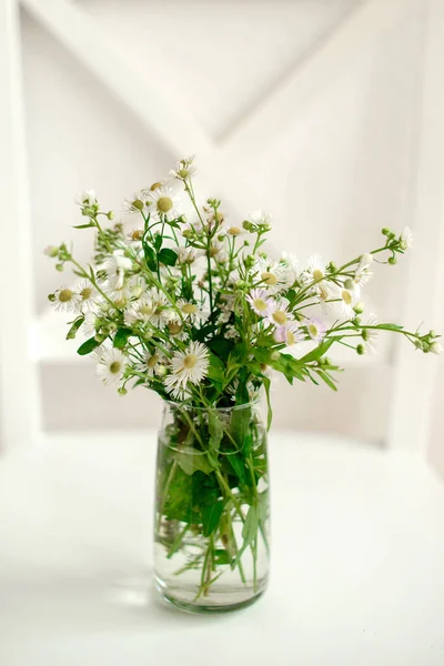A bouquet of field daisies in a glass vase on a bright wooden background. Decorating with family table flowers