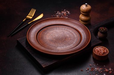 Koyu kahverengi zemin üzerinde boş kahverengi bir seramik tabak. Yemek masası hazırlanıyor.