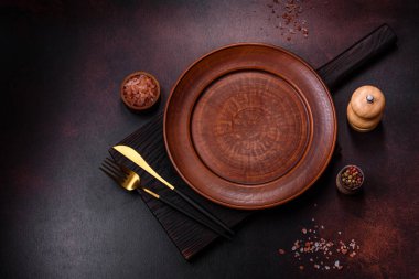 Koyu kahverengi zemin üzerinde boş kahverengi bir seramik tabak. Yemek masası hazırlanıyor.