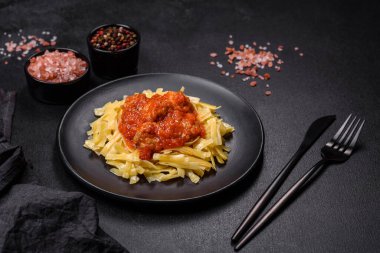 Köfteli spagetti siyah bir kasede domates sosu ile koyu beton arka planda.