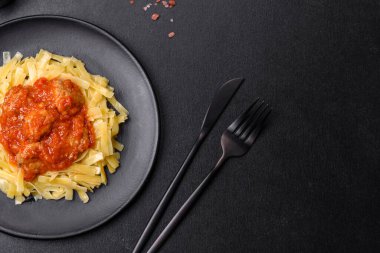 Köfteli spagetti siyah bir kasede domates sosu ile koyu beton arka planda.