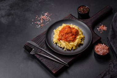 Köfteli spagetti siyah bir kasede domates sosu ile koyu beton arka planda.