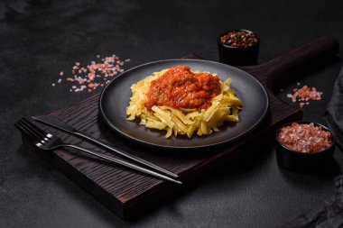 Köfteli spagetti siyah bir kasede domates sosu ile koyu beton arka planda.