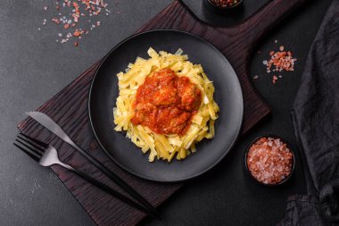 Köfteli spagetti siyah bir kasede domates sosu ile koyu beton arka planda.