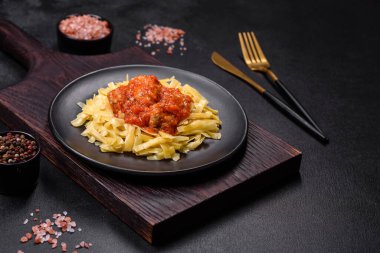 Köfteli spagetti siyah bir kasede domates sosu ile koyu beton arka planda.
