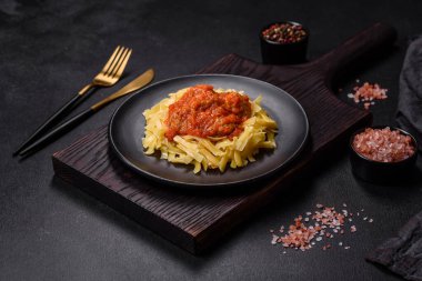 Köfteli spagetti siyah bir kasede domates sosu ile koyu beton arka planda.
