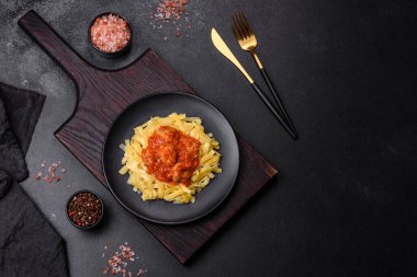 Köfteli spagetti siyah bir kasede domates sosu ile koyu beton arka planda.