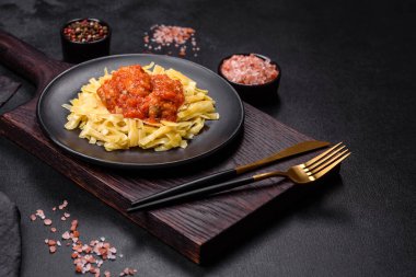 Köfteli spagetti siyah bir kasede domates sosu ile koyu beton arka planda.
